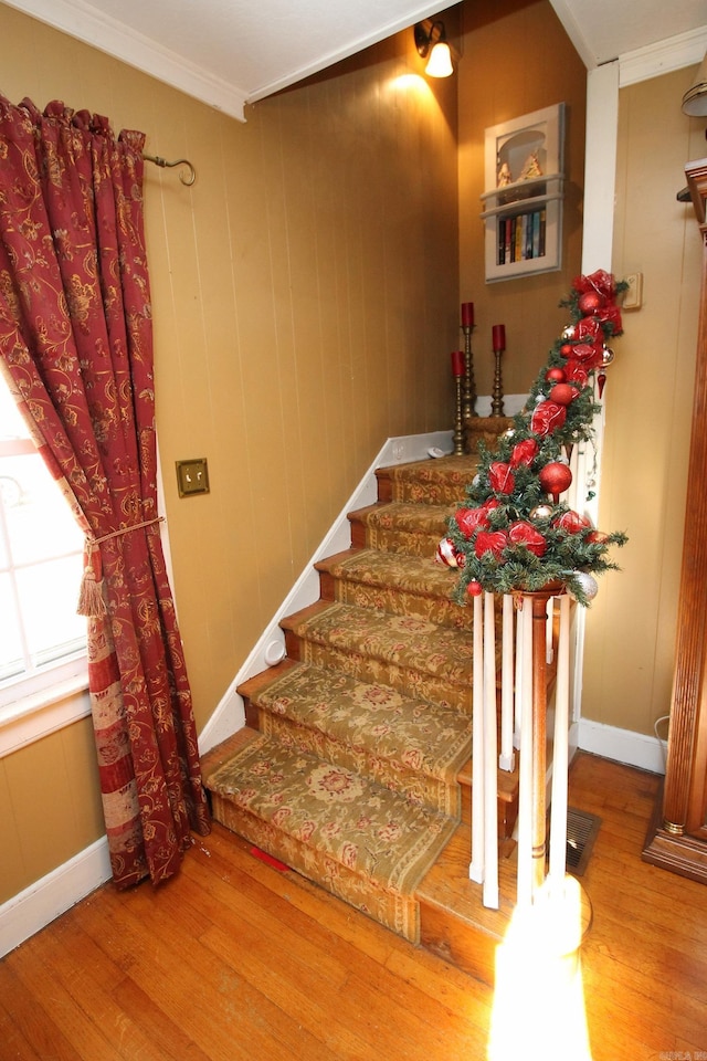 stairs with wood walls, wood-type flooring, and ornamental molding
