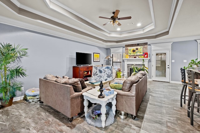 living room with a large fireplace, a raised ceiling, ceiling fan, and crown molding