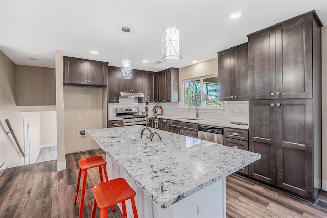 kitchen featuring stainless steel appliances, sink, wood-type flooring, decorative light fixtures, and a center island with sink