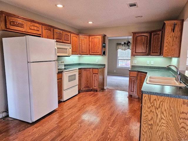 kitchen featuring sink, hanging light fixtures, a notable chandelier, wood-type flooring, and white appliances