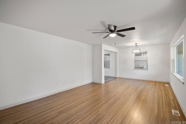 empty room with light hardwood / wood-style flooring and ceiling fan with notable chandelier