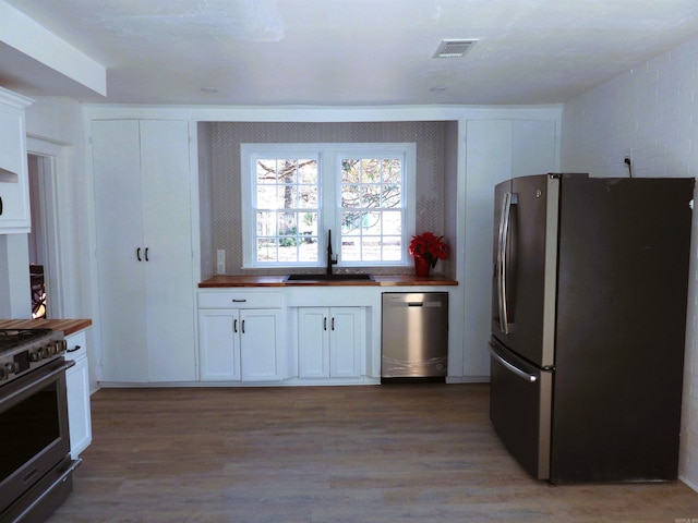 kitchen with appliances with stainless steel finishes, hardwood / wood-style flooring, white cabinetry, and sink