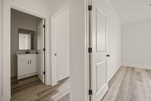 hallway featuring light wood-type flooring, ornamental molding, and sink