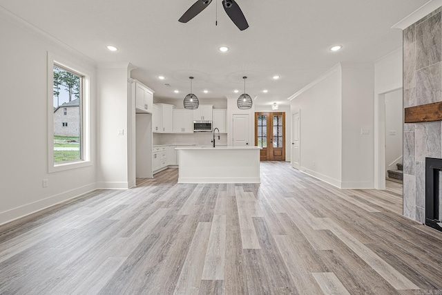 unfurnished living room featuring sink, ceiling fan, light wood-type flooring, a fireplace, and ornamental molding