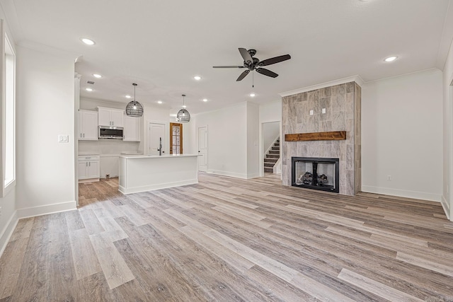 unfurnished living room with a fireplace, light hardwood / wood-style flooring, ceiling fan, and ornamental molding