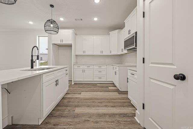 kitchen featuring decorative light fixtures, wood-type flooring, white cabinetry, and sink