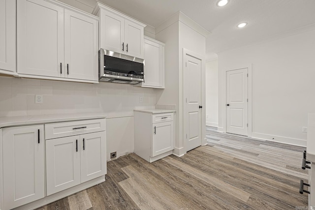 kitchen featuring tasteful backsplash, white cabinetry, light hardwood / wood-style flooring, and crown molding