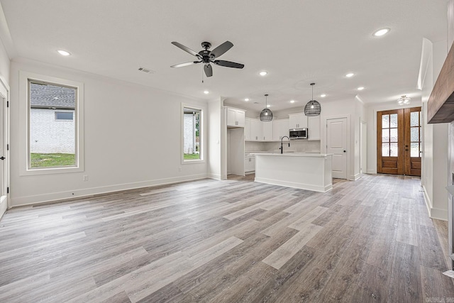 unfurnished living room with a healthy amount of sunlight, french doors, and light hardwood / wood-style flooring