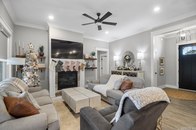 living room featuring a fireplace, light wood-type flooring, ceiling fan, and ornamental molding