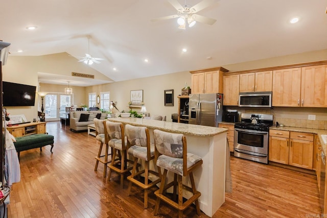 kitchen featuring appliances with stainless steel finishes, light wood-type flooring, light stone counters, a breakfast bar area, and lofted ceiling