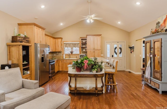 kitchen featuring light brown cabinetry, stainless steel appliances, vaulted ceiling, and hardwood / wood-style flooring