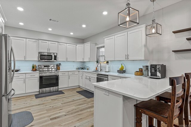 kitchen with kitchen peninsula, white cabinets, pendant lighting, stainless steel appliances, and backsplash