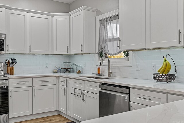 kitchen featuring sink, appliances with stainless steel finishes, white cabinetry, light stone countertops, and decorative backsplash