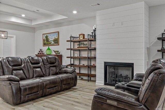 living room featuring a raised ceiling, a large fireplace, a textured ceiling, and light hardwood / wood-style floors