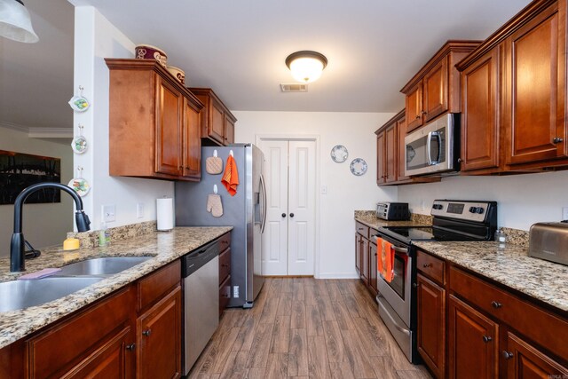 kitchen featuring sink, stainless steel appliances, light stone counters, crown molding, and light hardwood / wood-style floors