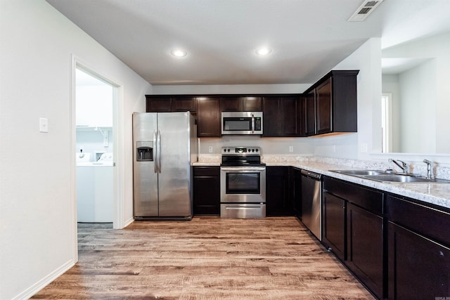 kitchen featuring appliances with stainless steel finishes, light stone counters, dark brown cabinetry, sink, and light hardwood / wood-style flooring