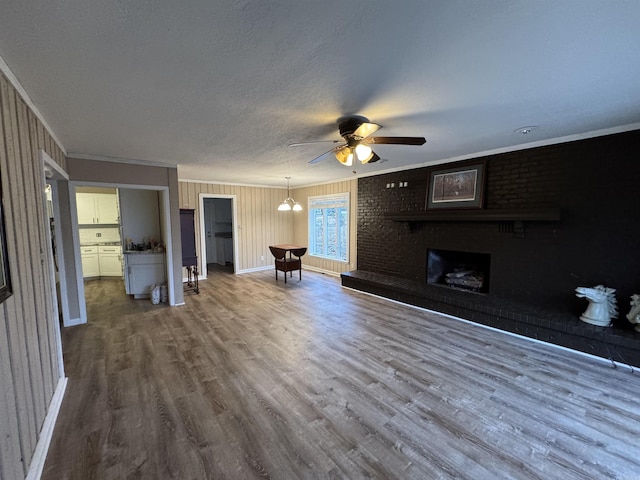 unfurnished living room with a brick fireplace, crown molding, wood-type flooring, a textured ceiling, and ceiling fan with notable chandelier