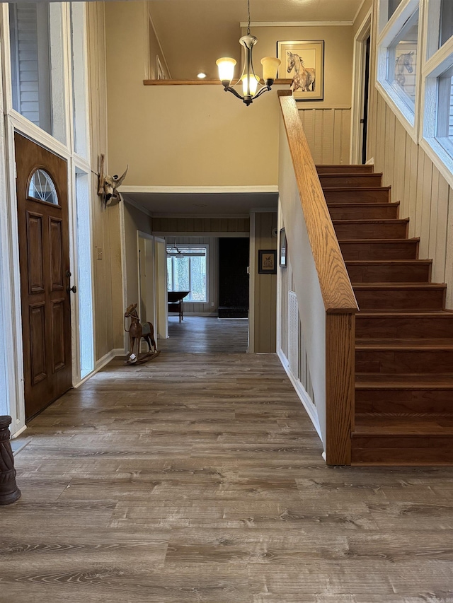 entrance foyer with hardwood / wood-style floors, a towering ceiling, ornamental molding, and a notable chandelier