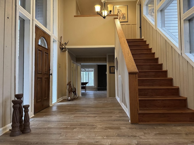 stairway featuring wooden walls, wood-type flooring, and an inviting chandelier