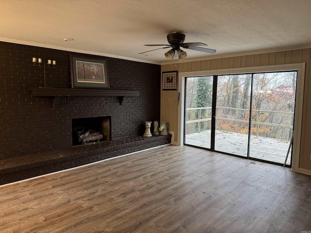 unfurnished living room featuring a brick fireplace, ornamental molding, a textured ceiling, ceiling fan, and hardwood / wood-style flooring