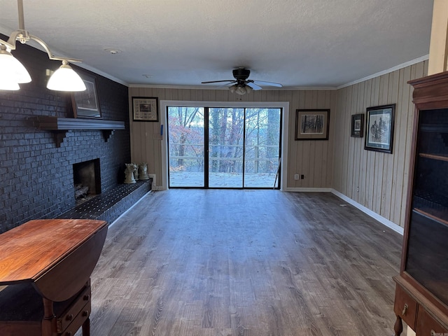 unfurnished living room featuring wood-type flooring, a brick fireplace, ceiling fan, and ornamental molding