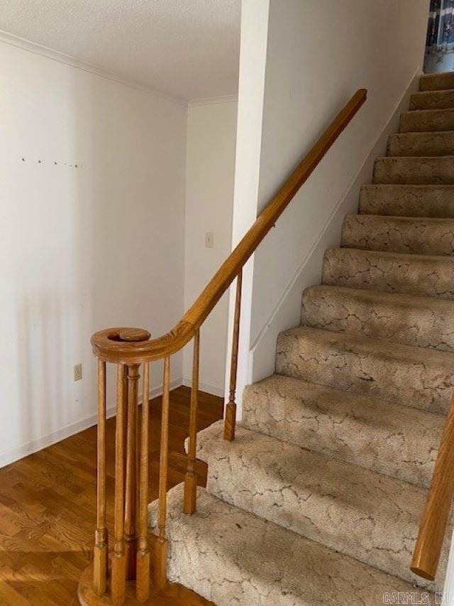 staircase featuring hardwood / wood-style floors, ornamental molding, and a textured ceiling