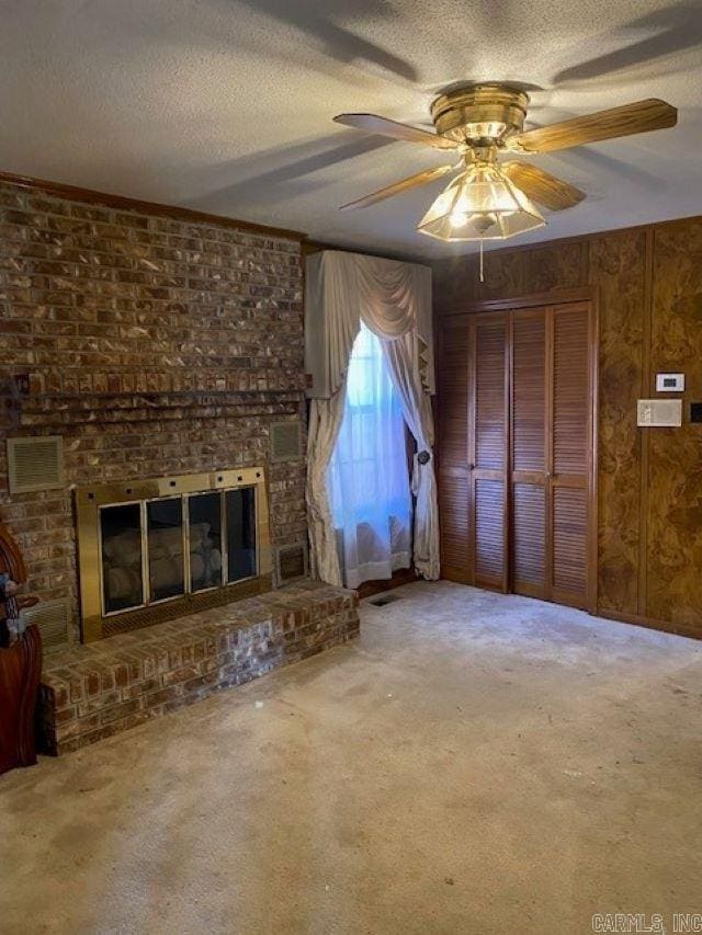 unfurnished living room with wood walls, a brick fireplace, ceiling fan, a textured ceiling, and carpet floors