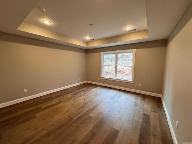 empty room with dark hardwood / wood-style flooring and a tray ceiling