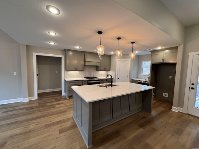 kitchen with sink, gray cabinetry, decorative light fixtures, a center island with sink, and stainless steel range