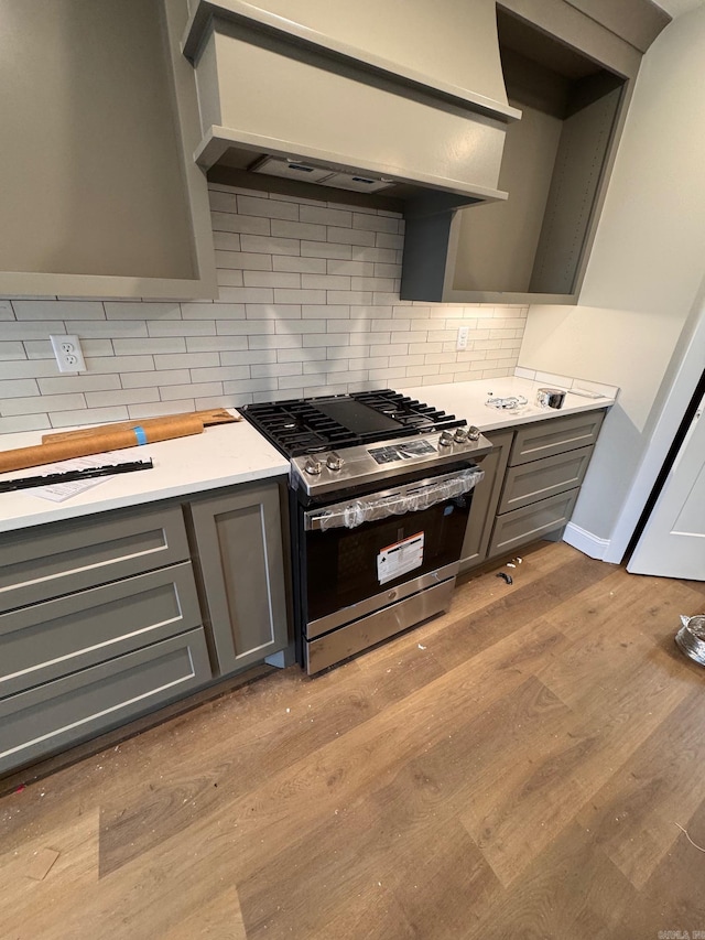 kitchen with decorative backsplash, gray cabinets, gas stove, and custom range hood