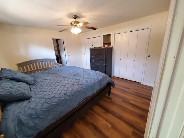 bedroom with a textured ceiling, ceiling fan, dark wood-type flooring, and two closets