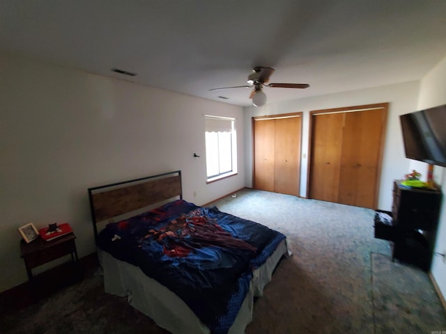 bedroom with ceiling fan, dark carpet, and multiple closets