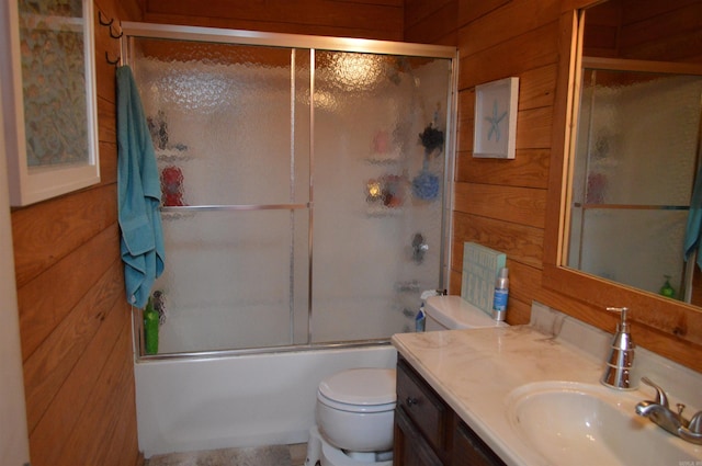 bathroom featuring wooden walls, toilet, vanity, and shower / bath combination with glass door