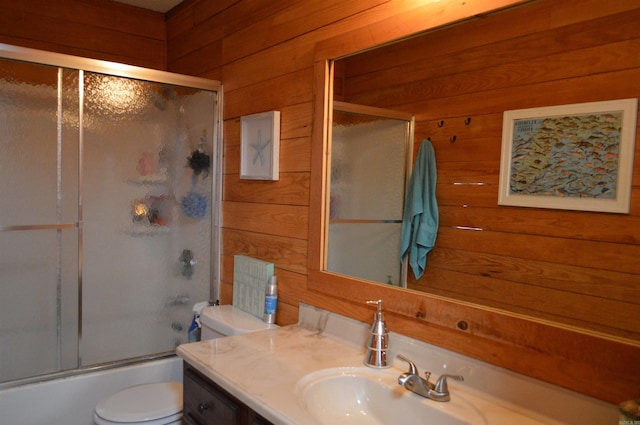 bathroom with wood walls, toilet, vanity, and shower / bath combination with glass door