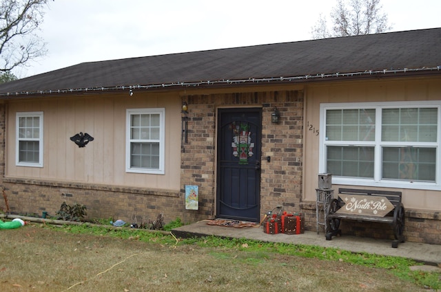 doorway to property with brick siding and a shingled roof