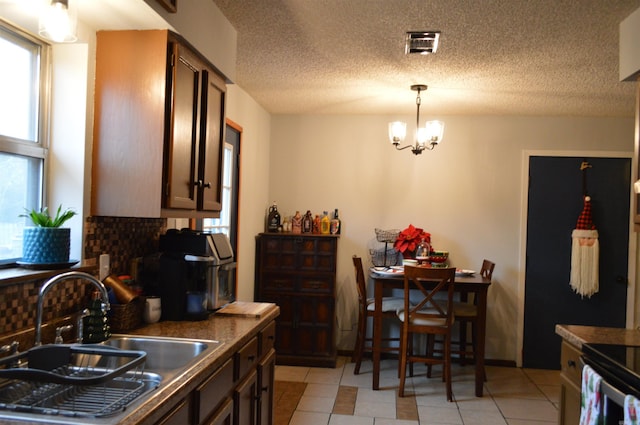 kitchen featuring visible vents, a sink, dark countertops, backsplash, and an inviting chandelier