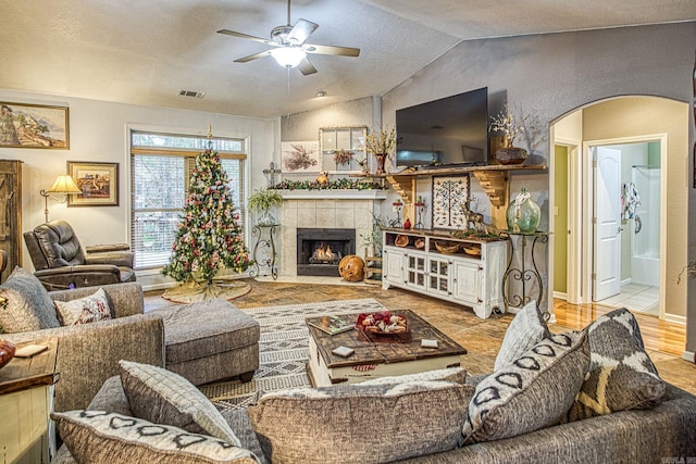 living room featuring a textured ceiling, vaulted ceiling, ceiling fan, light hardwood / wood-style flooring, and a tiled fireplace