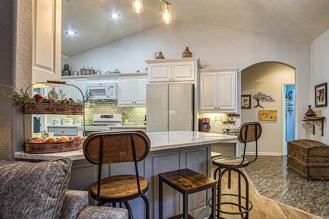 kitchen featuring lofted ceiling, stainless steel built in fridge, hardwood / wood-style flooring, light stone counters, and range