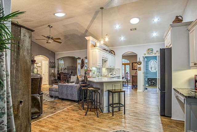 kitchen with wood-type flooring, vaulted ceiling, a kitchen bar, white cabinetry, and stainless steel appliances