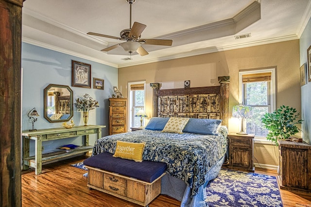 bedroom with wood-type flooring, a raised ceiling, ceiling fan, and crown molding