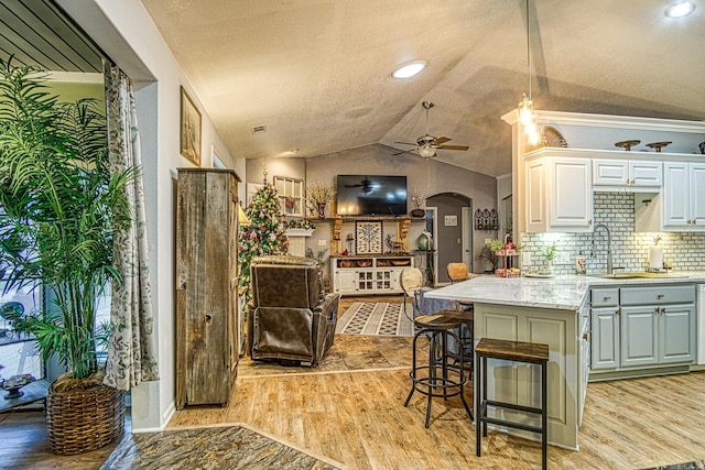 kitchen with vaulted ceiling, ceiling fan, light hardwood / wood-style flooring, white cabinets, and a breakfast bar area