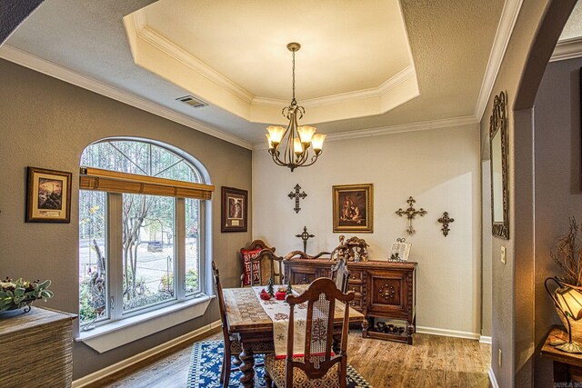 dining room with hardwood / wood-style flooring, a raised ceiling, crown molding, and a chandelier