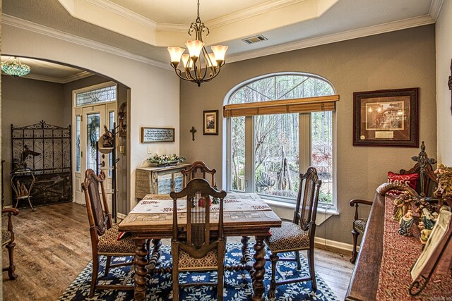 dining area featuring hardwood / wood-style floors, an inviting chandelier, a raised ceiling, and crown molding