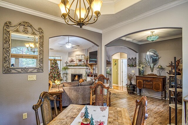 dining space featuring hardwood / wood-style floors, a fireplace, crown molding, and ceiling fan with notable chandelier