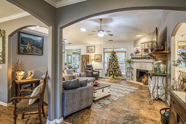 living room with a tile fireplace, ceiling fan, crown molding, and lofted ceiling