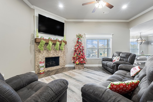 living room featuring hardwood / wood-style floors, ceiling fan with notable chandelier, crown molding, and a brick fireplace