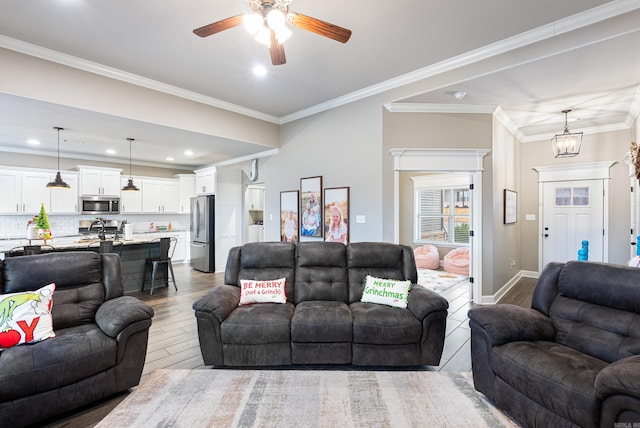 living room featuring crown molding, sink, ceiling fan with notable chandelier, and light wood-type flooring