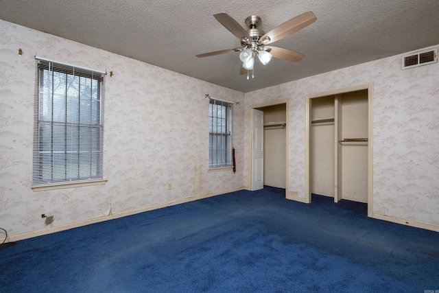 unfurnished bedroom with dark colored carpet, a textured ceiling, ceiling fan, and multiple closets