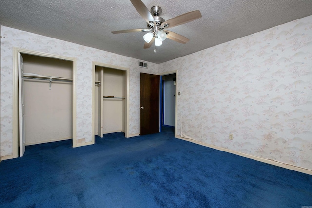 unfurnished bedroom with multiple closets, ceiling fan, dark carpet, and a textured ceiling