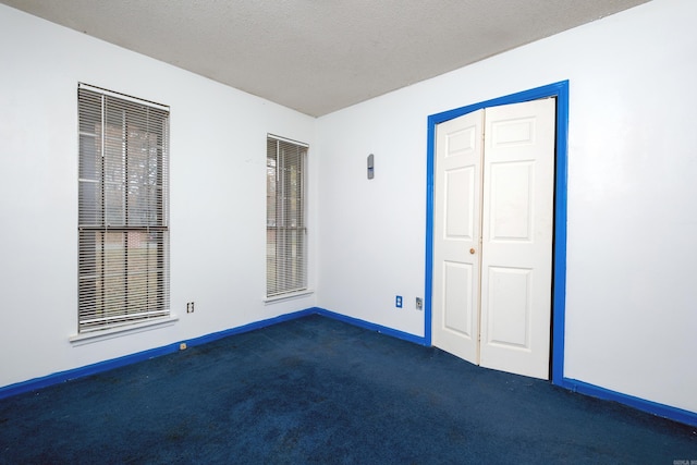 unfurnished bedroom with dark colored carpet, a textured ceiling, and a closet